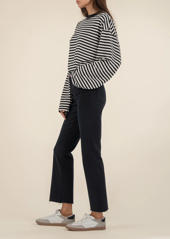 Woman turned to the side wearing black jeans with a black and white striped sweater and white sneakers standing in front of a white background