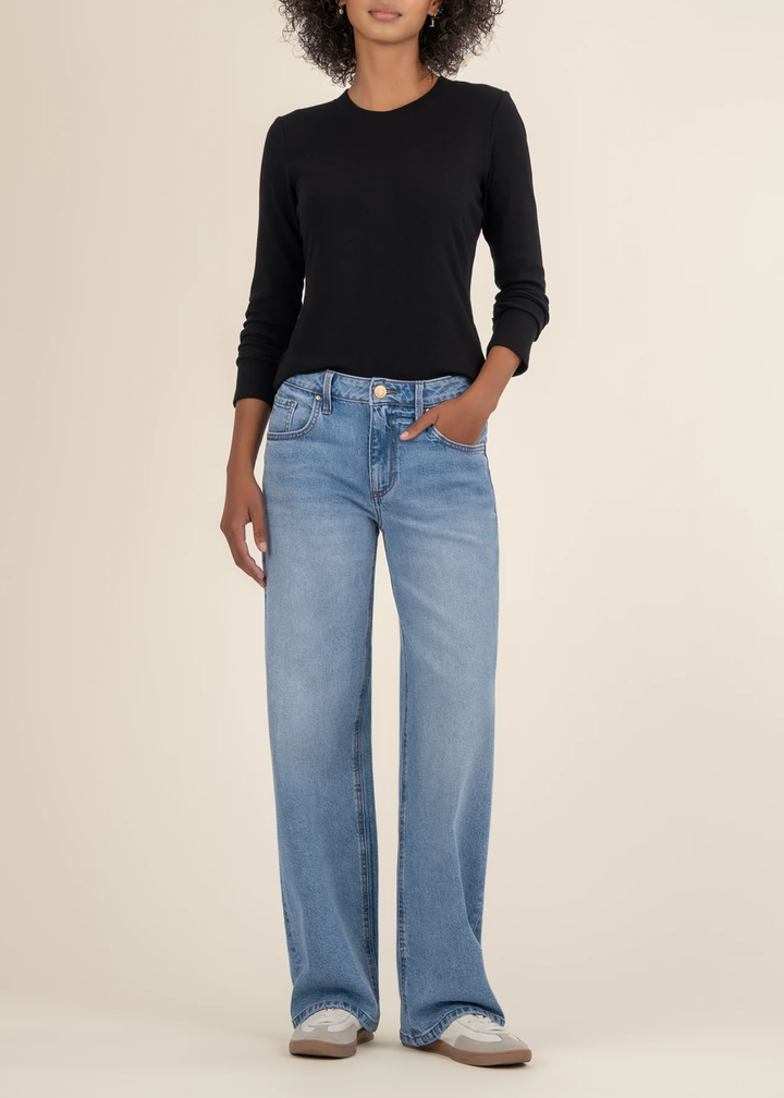 Woman wearing a black long sleeve tee with jeans and white sneakers in front of a white background