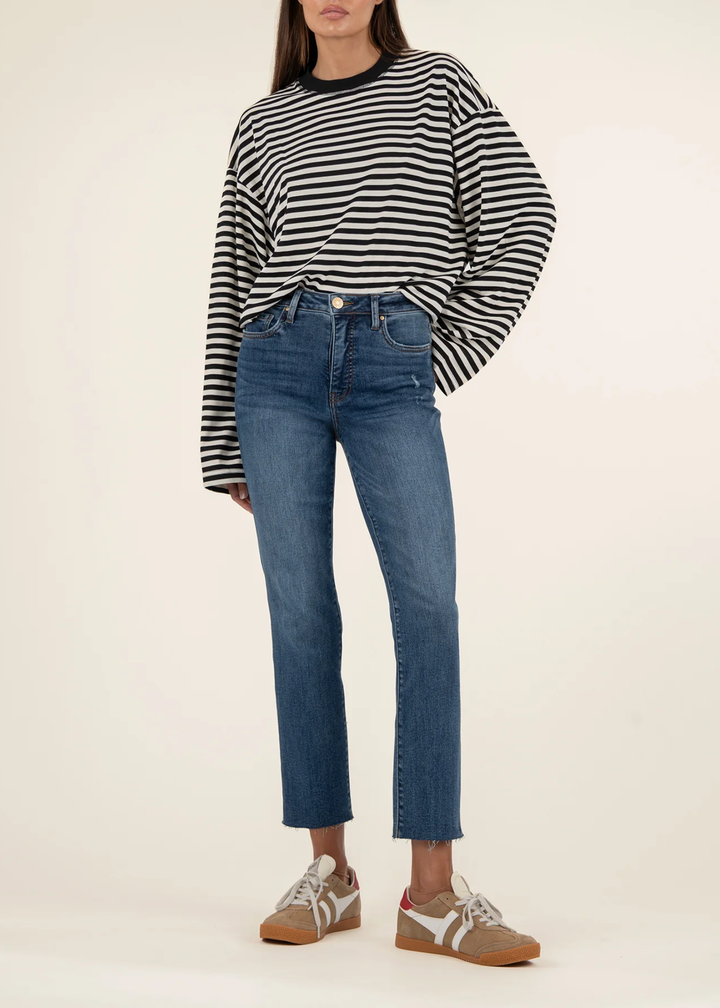 Woman wearing medium wash blue ankle straight jeans with tan sneakers and a black and white striped sweater standing in front of a white background