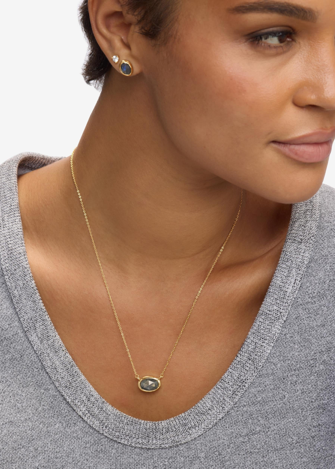Woman wearing a gold framed labradorite pendant necklace with matching earrings