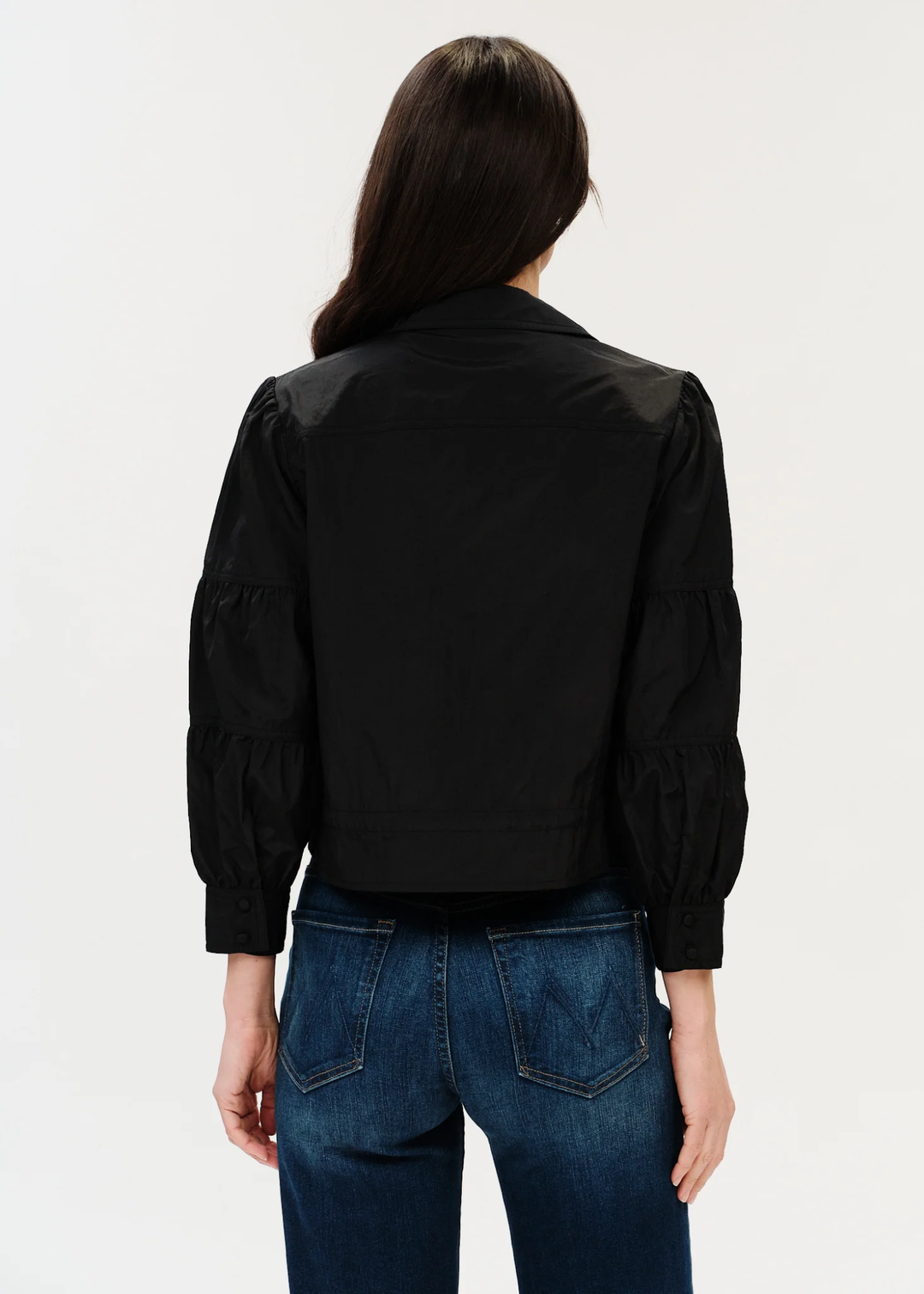 Woman with dark hair posing in black jacket turned around.