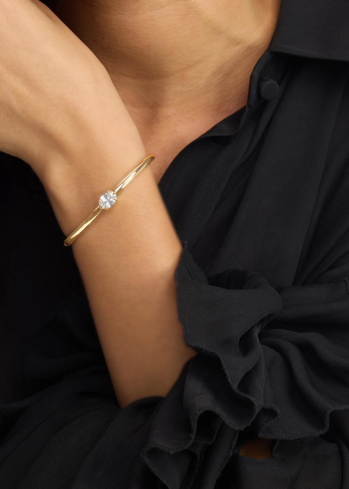 Close up of a woman wearing a gold cuff bracelet with a diamond stud
