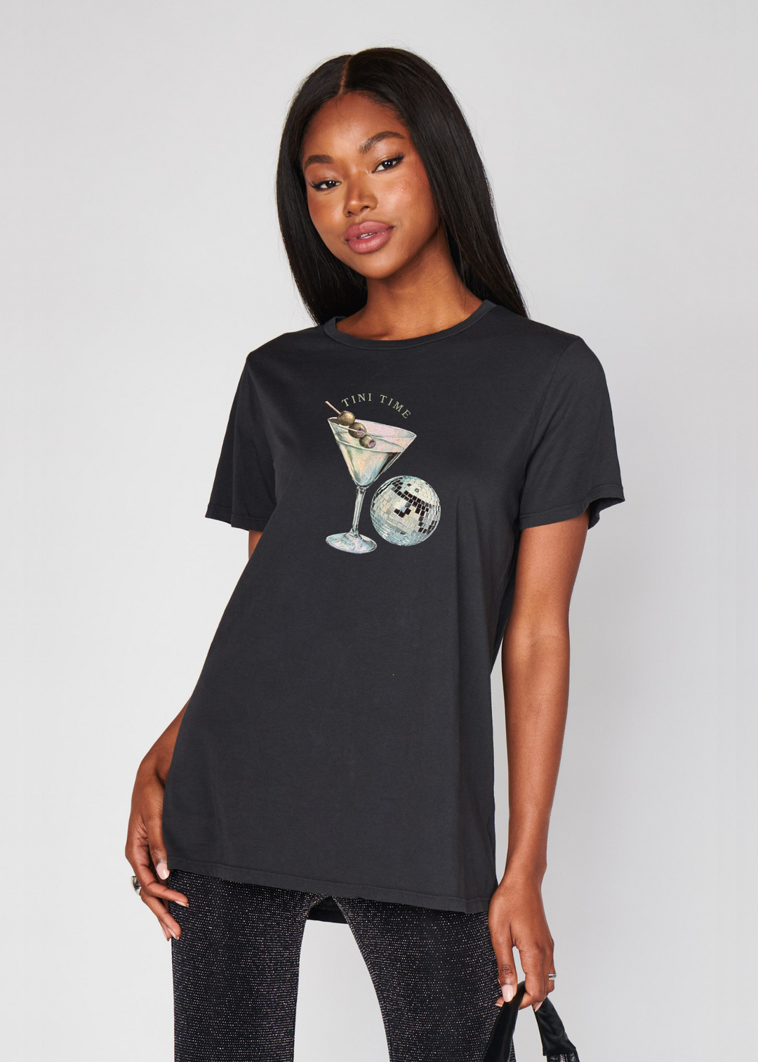 Woman wearing a charcoal grey shirt with a martini and disco ball graphic and that says "Tini Time"