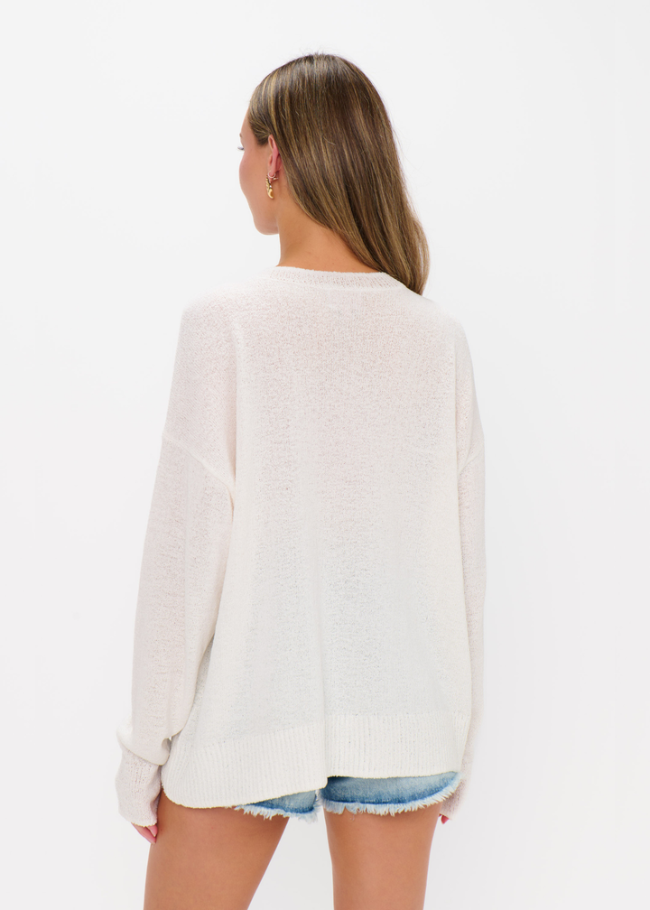 Woman turned around wearing a white sweater and denim shorts against a white background