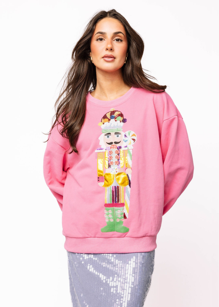 Woman wearing a pink sweatshirt with a sequin nutcracker graphic with a grey sequin skirt in front of a white background