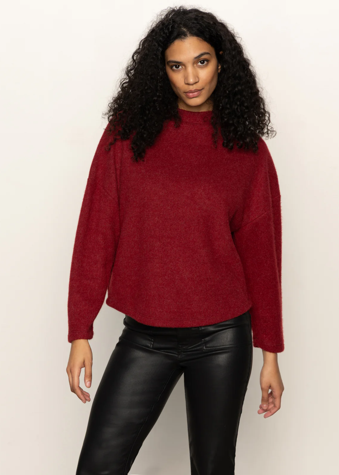 Woman wearing a crimson red sweater with black pants standing in front of a white background