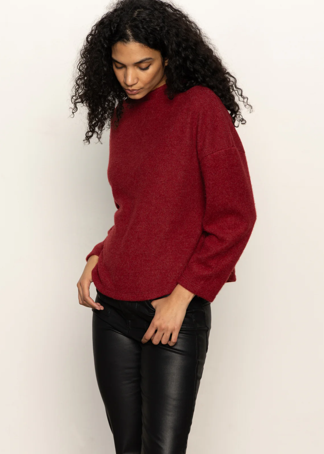 Woman wearing a crimson red sweater with black pants standing in front of a white background