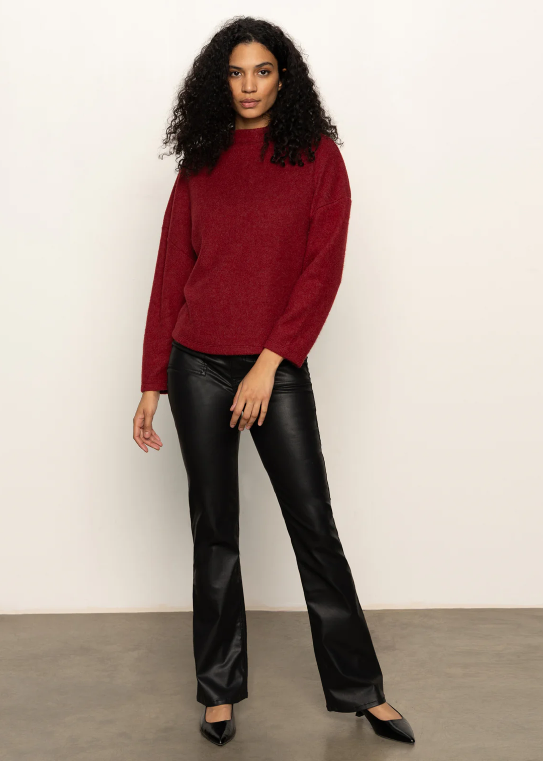Woman wearing a crimson red sweater with black pants standing in front of a white background