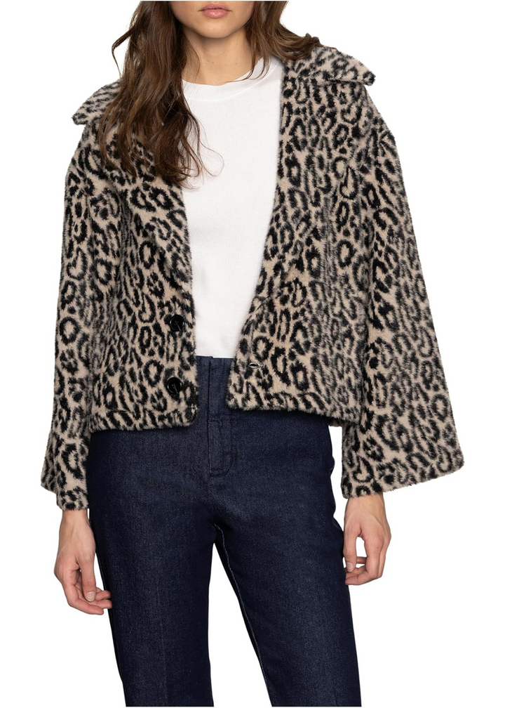 Woman wearing a leopard print faux fur jacket over a white shirt and black pants standing in front of a white background