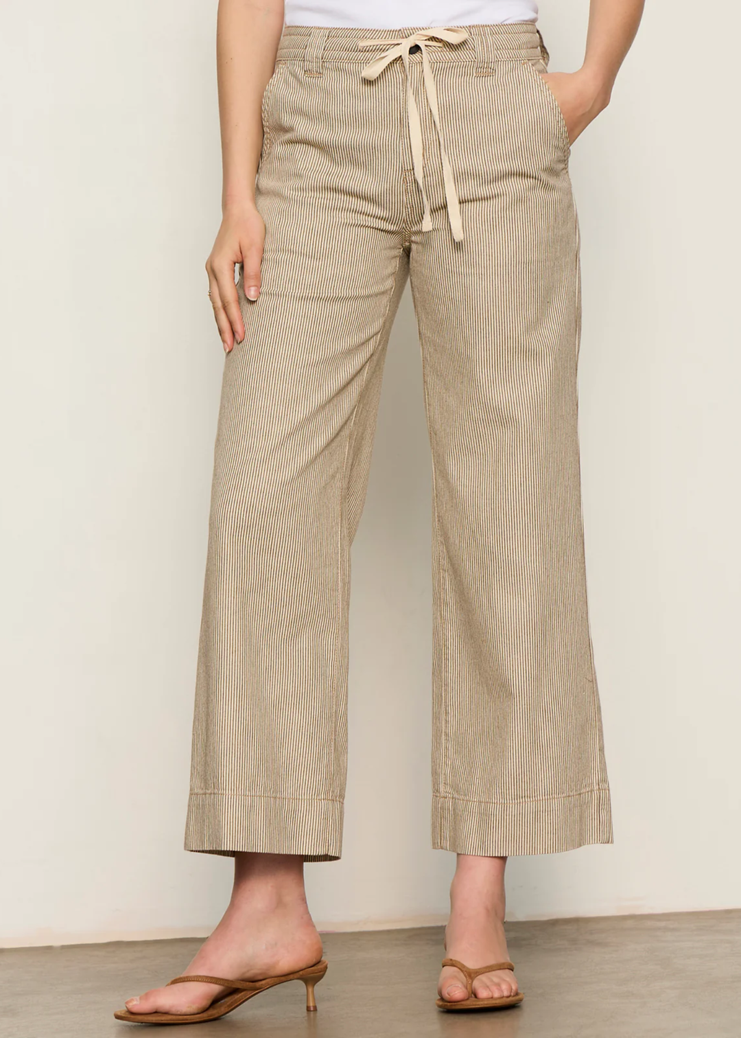 Woman wearing brown and white striped wide leg pants with sandals and a white tank top