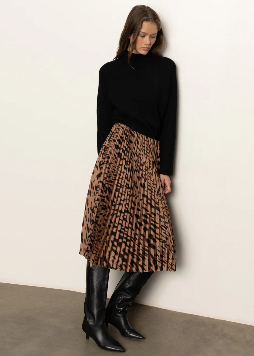 Woman wearing a black turtleneck sweater with a pleated leopard print midi skirt and tall black boots
