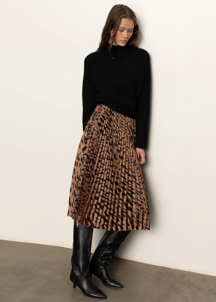 Woman wearing a black turtleneck sweater with a pleated leopard print midi skirt and tall black boots