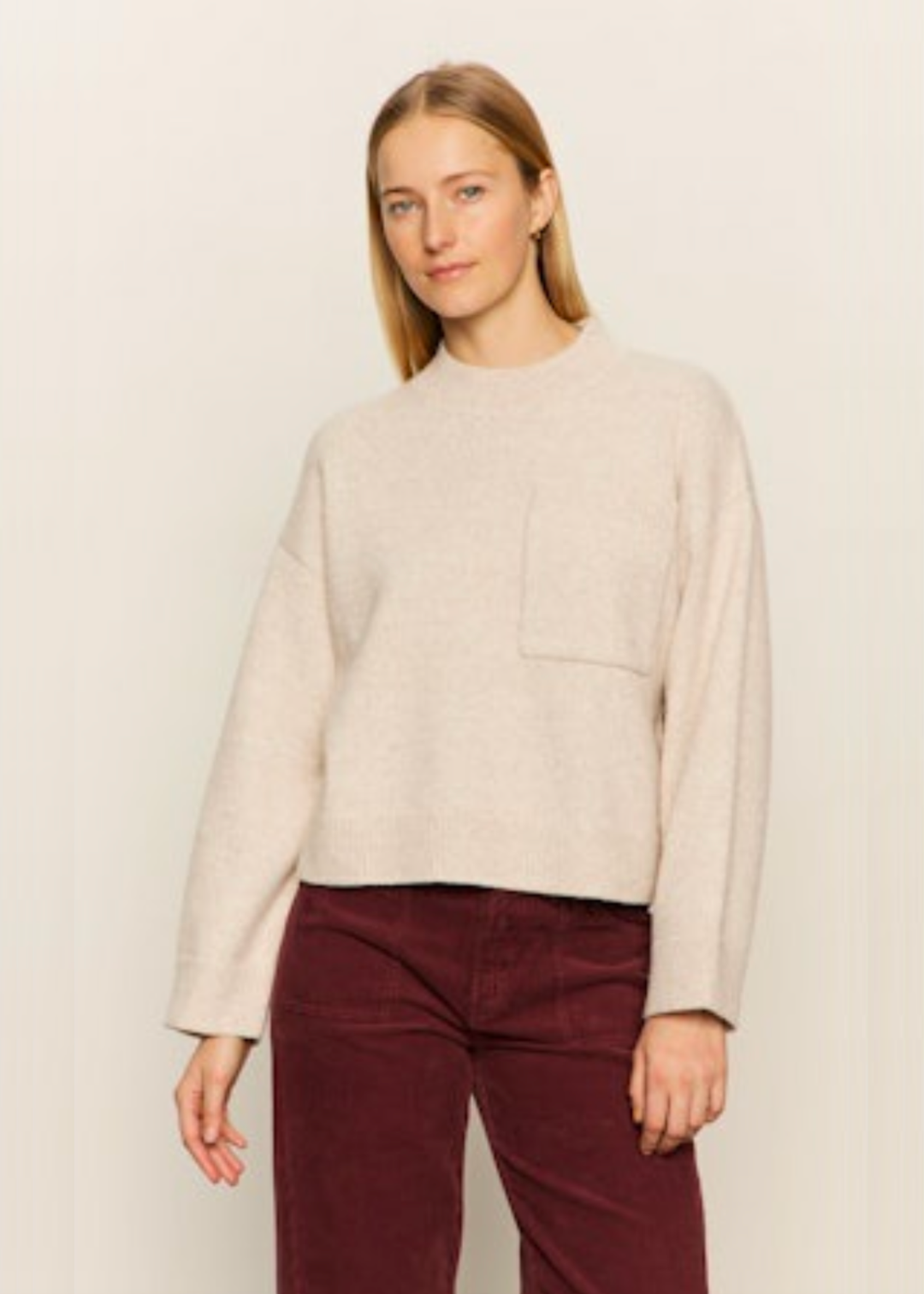 Woman wearing a cream crewneck sweater with a front pocket