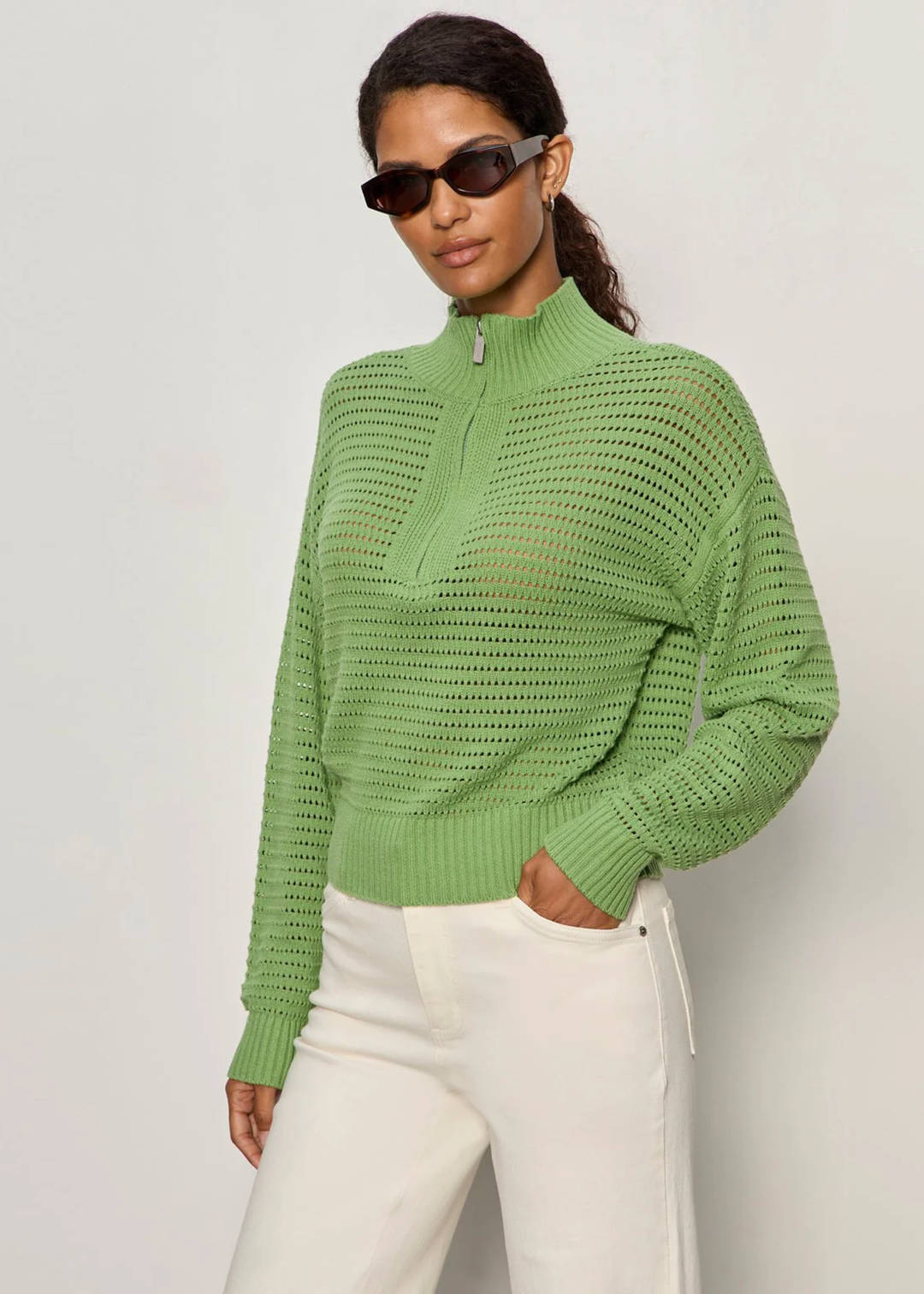 Woman with hand in pocket wearing a green knit half zip sweater with cream jeans