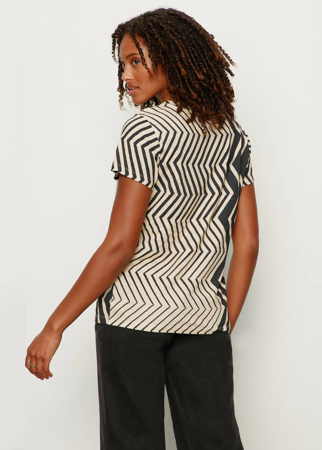 Woman turned around wearing a t-shirt with white and black zig zag stripes with black jeans