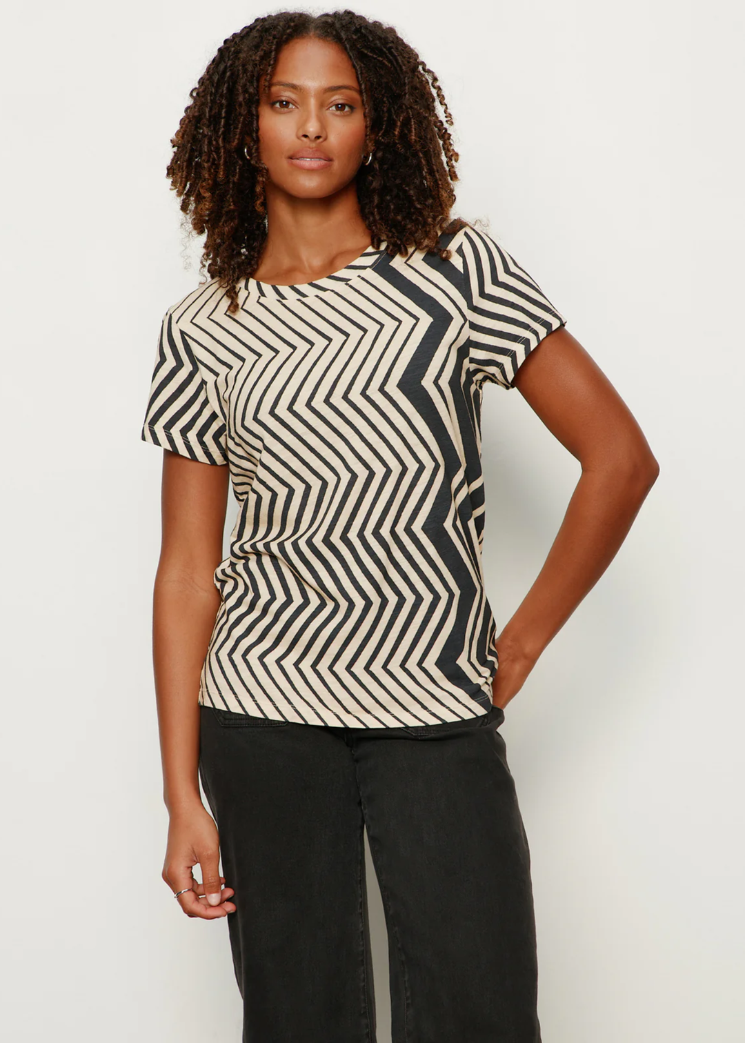 Woman with hand in pocket wearing a t-shirt with white and black zig zag stripes with black jeans