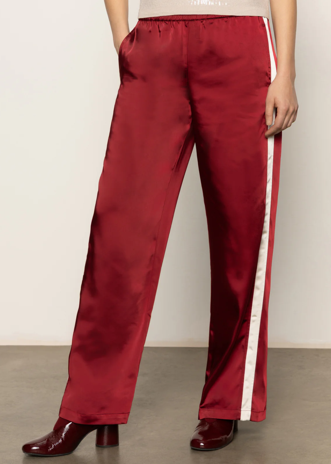 Woman wearing red satin pants with a white side stripe and black boots