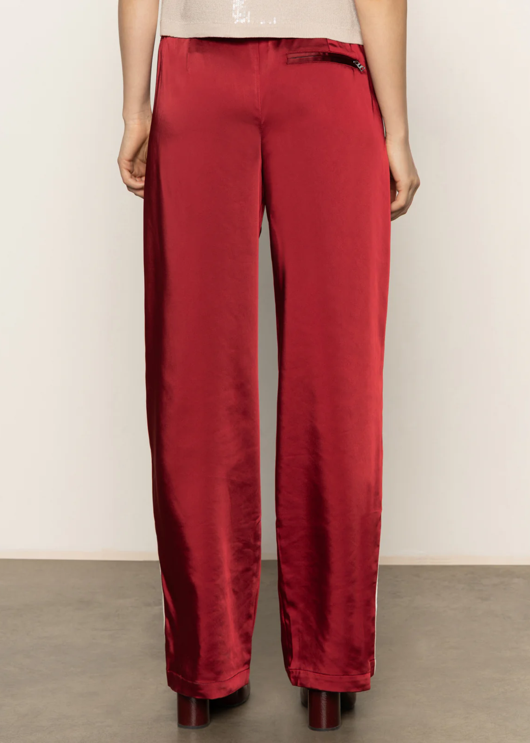 Woman turned around wearing red satin pants with a white side stripe and black boots