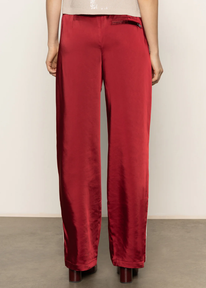 Woman turned around wearing red satin pants with a white side stripe and black boots