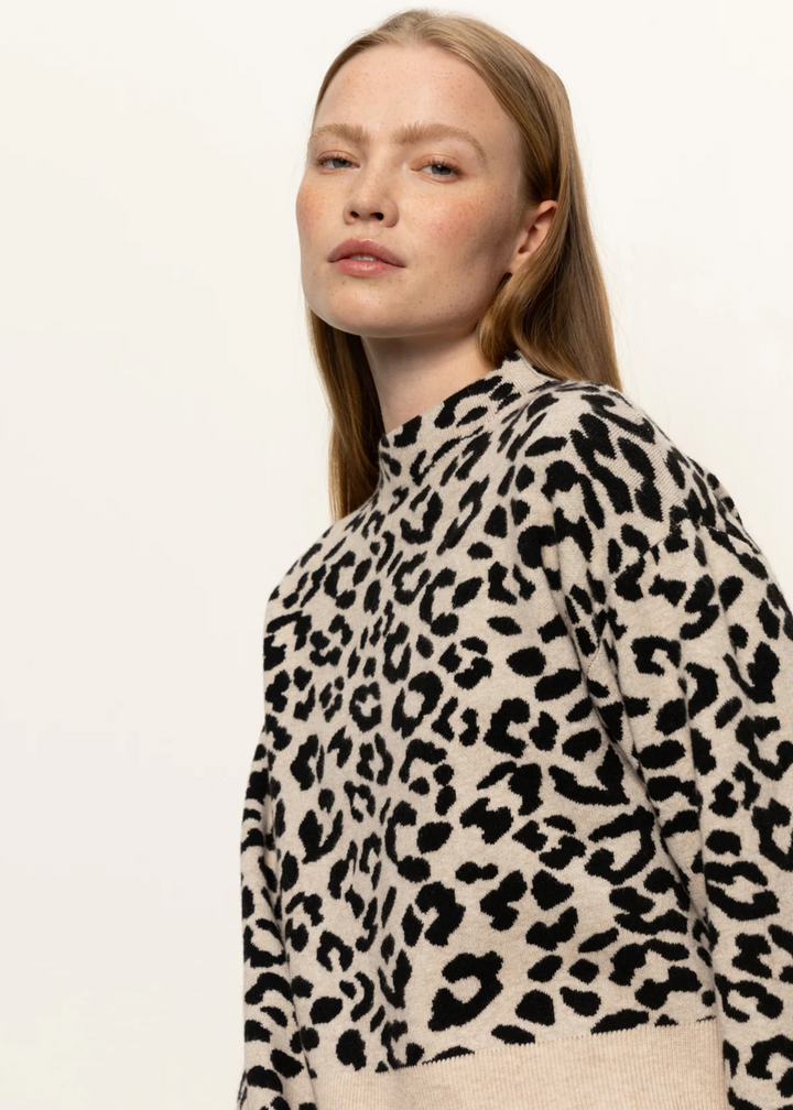 Woman wearing a tan and black leopard print mock neck sweater in front of a white background