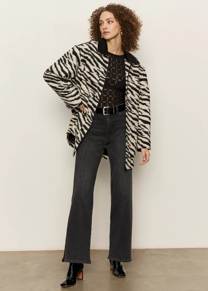 Woman with hand on hip wearing a white and black zebra print barn jacket with black washed jeans against a white background