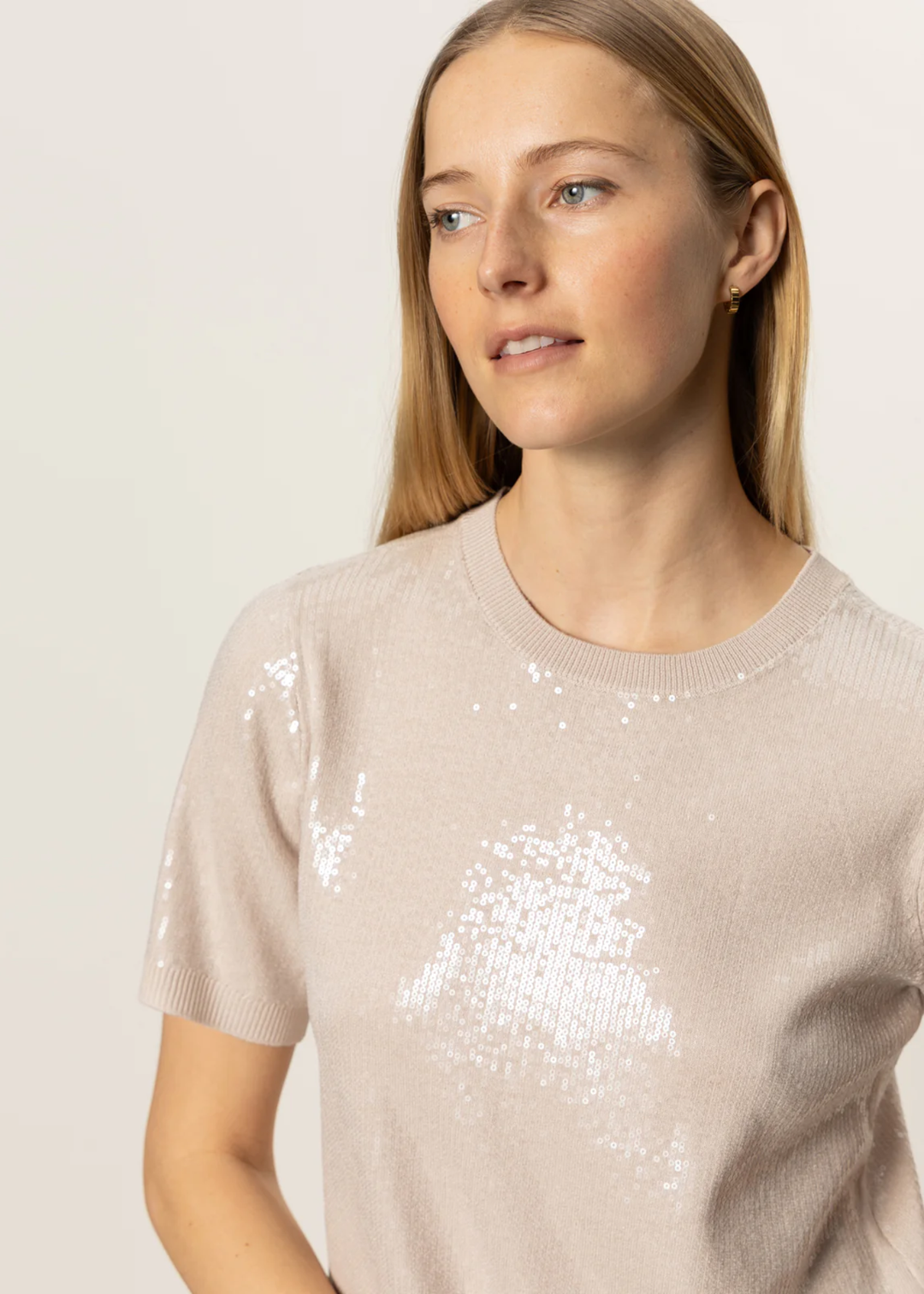 Close up of a woman wearing a cream sequin short sleeve top