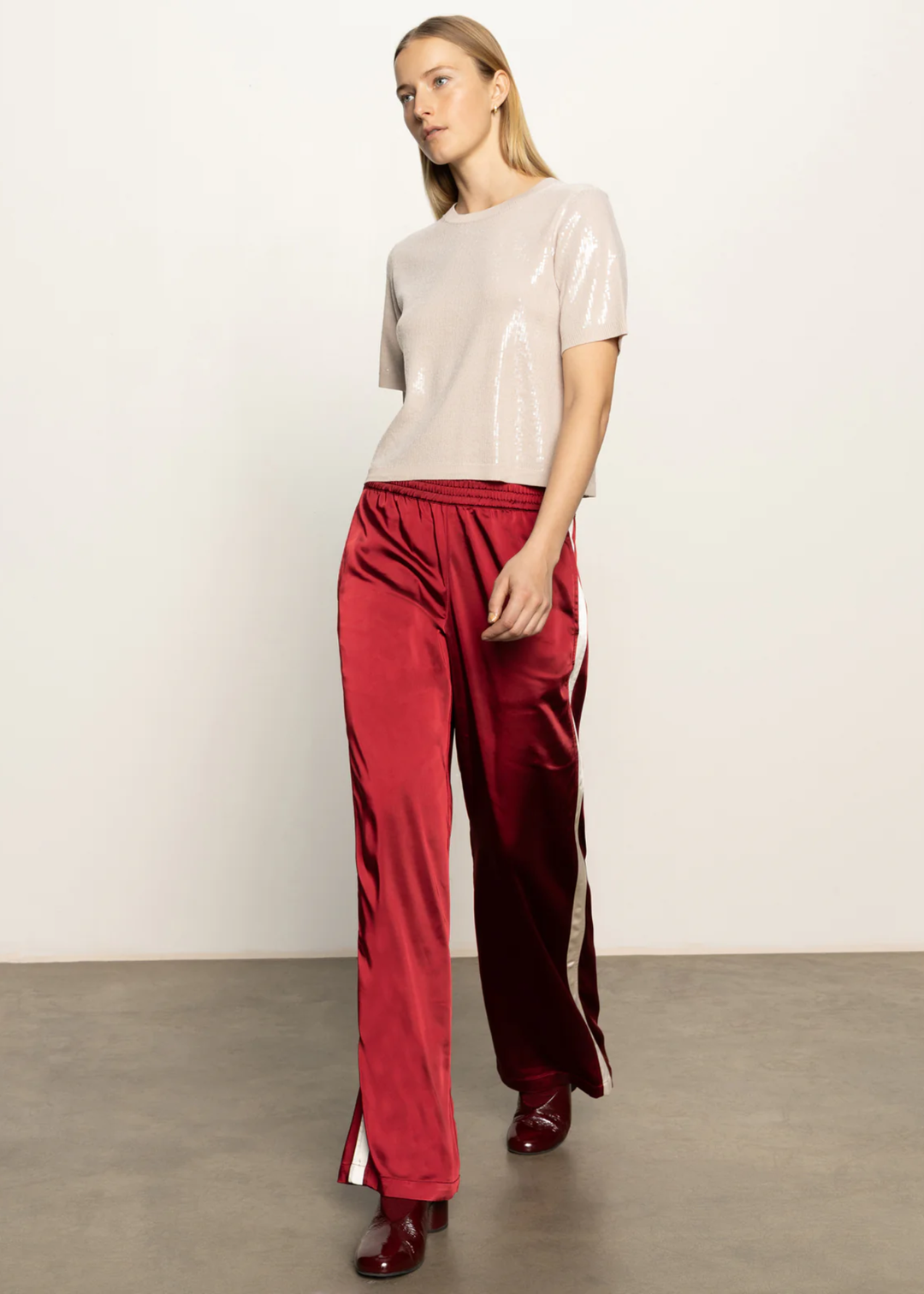 Woman wearing a cream sequined short sleeve top with red satin pants standing in front of a white background