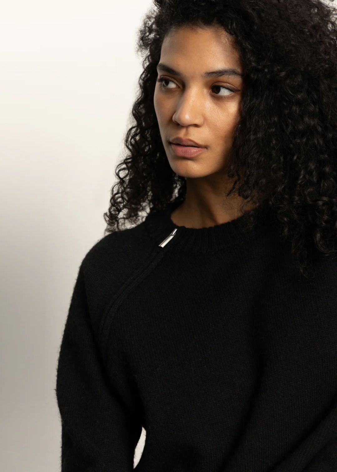 Close up of a woman wearing a black sweater with a silver zipper at the neckline