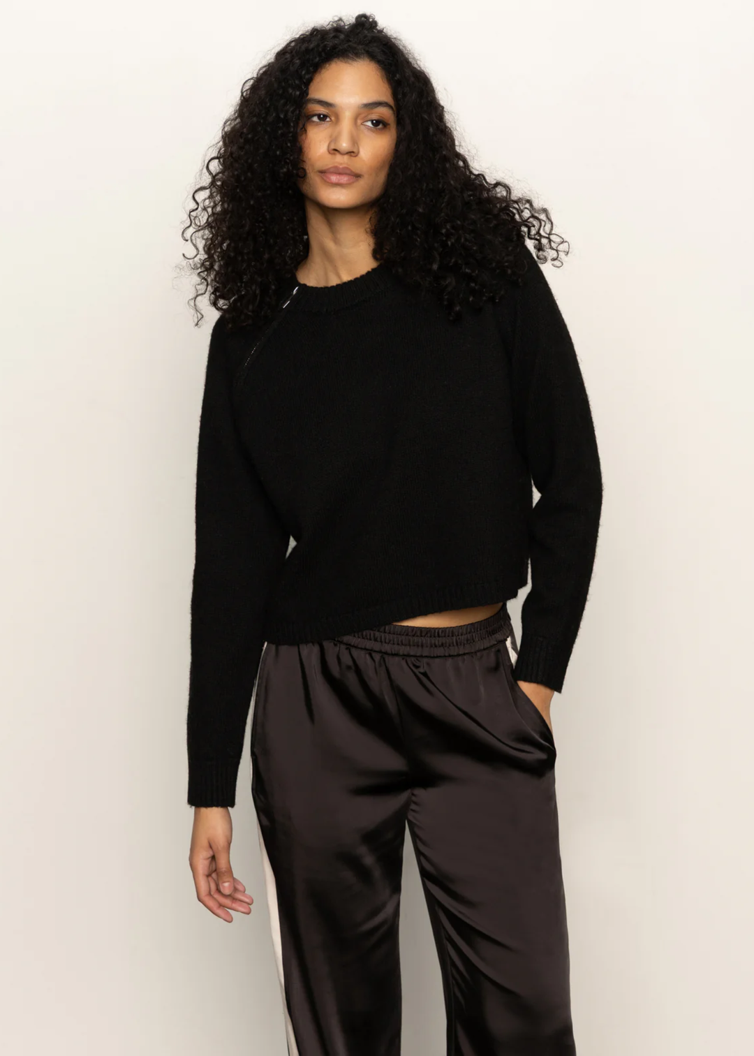 Woman wearing a black sweater and black pants standing in front of a white background