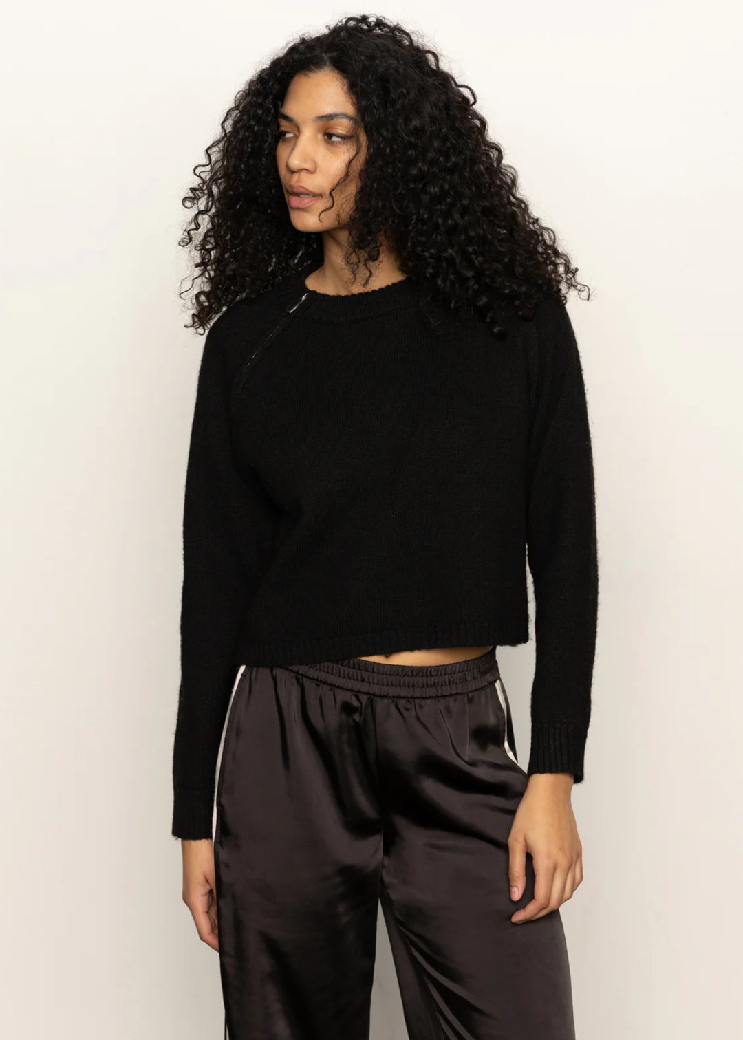 Woman wearing a black sweater and black pants standing in front of a white background