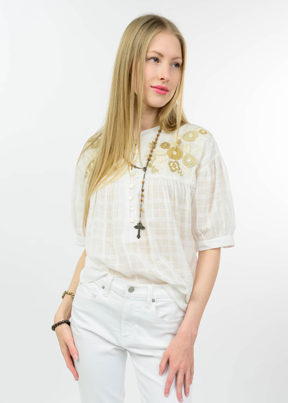 Woman wearing a white top with floral embroidery on the top and white jeans