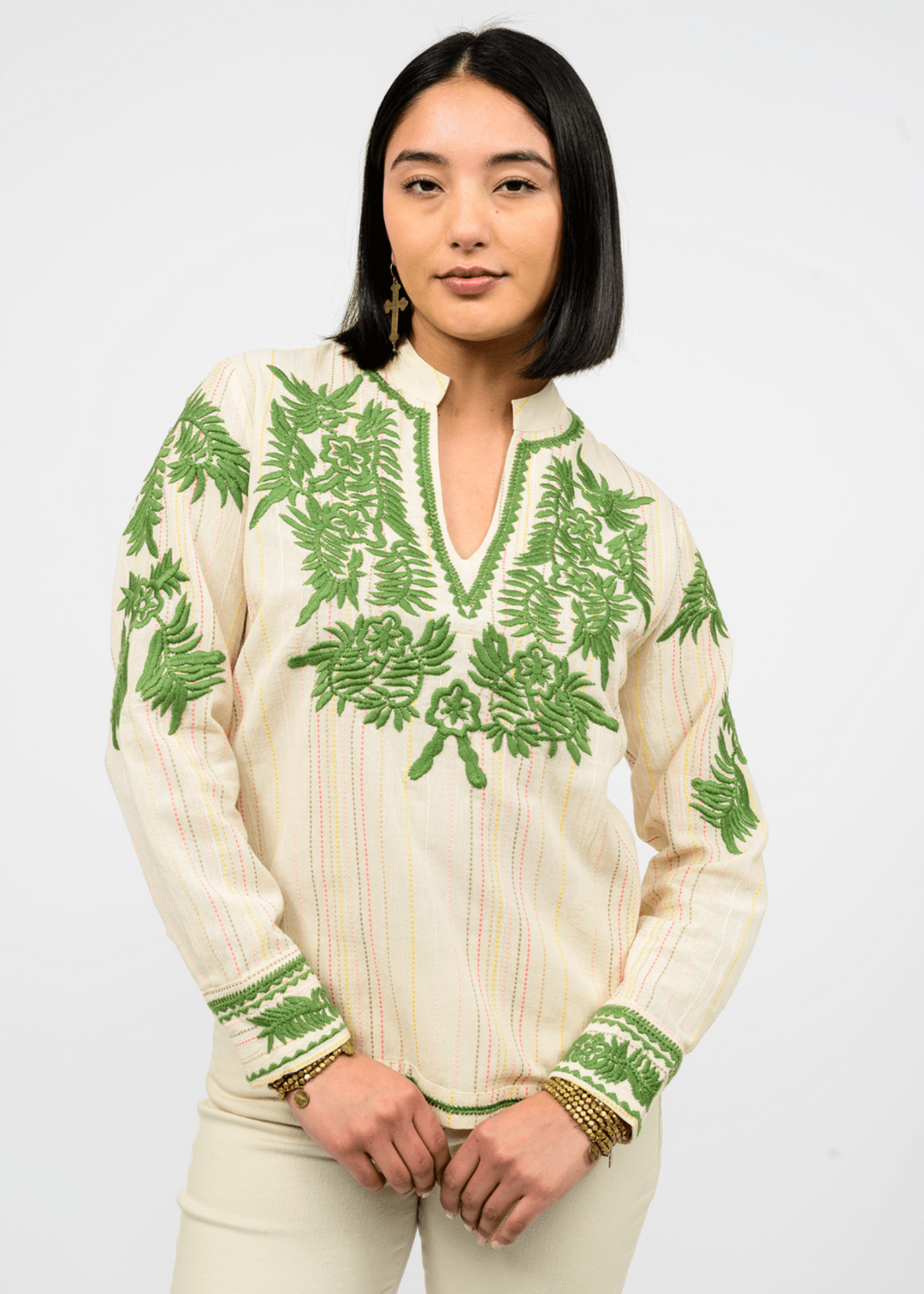 Woman wearing a long sleeve, ivory top with a v-neck and green floral embroidery in front of a white background