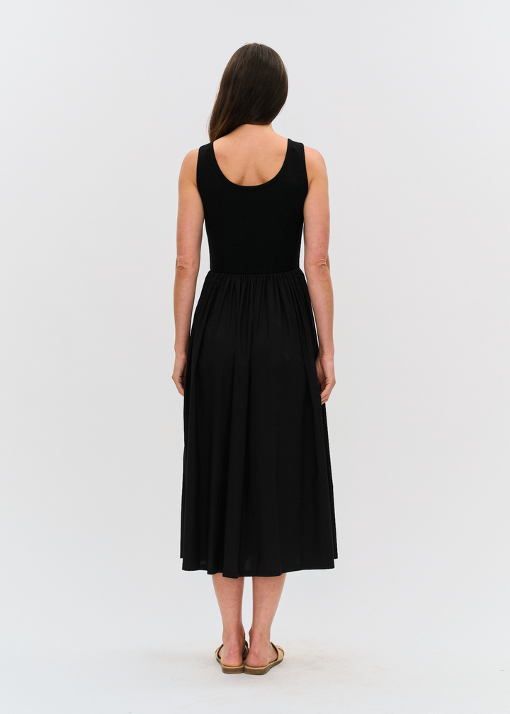 Woman turned around wearing a black midi dress with tan sandals