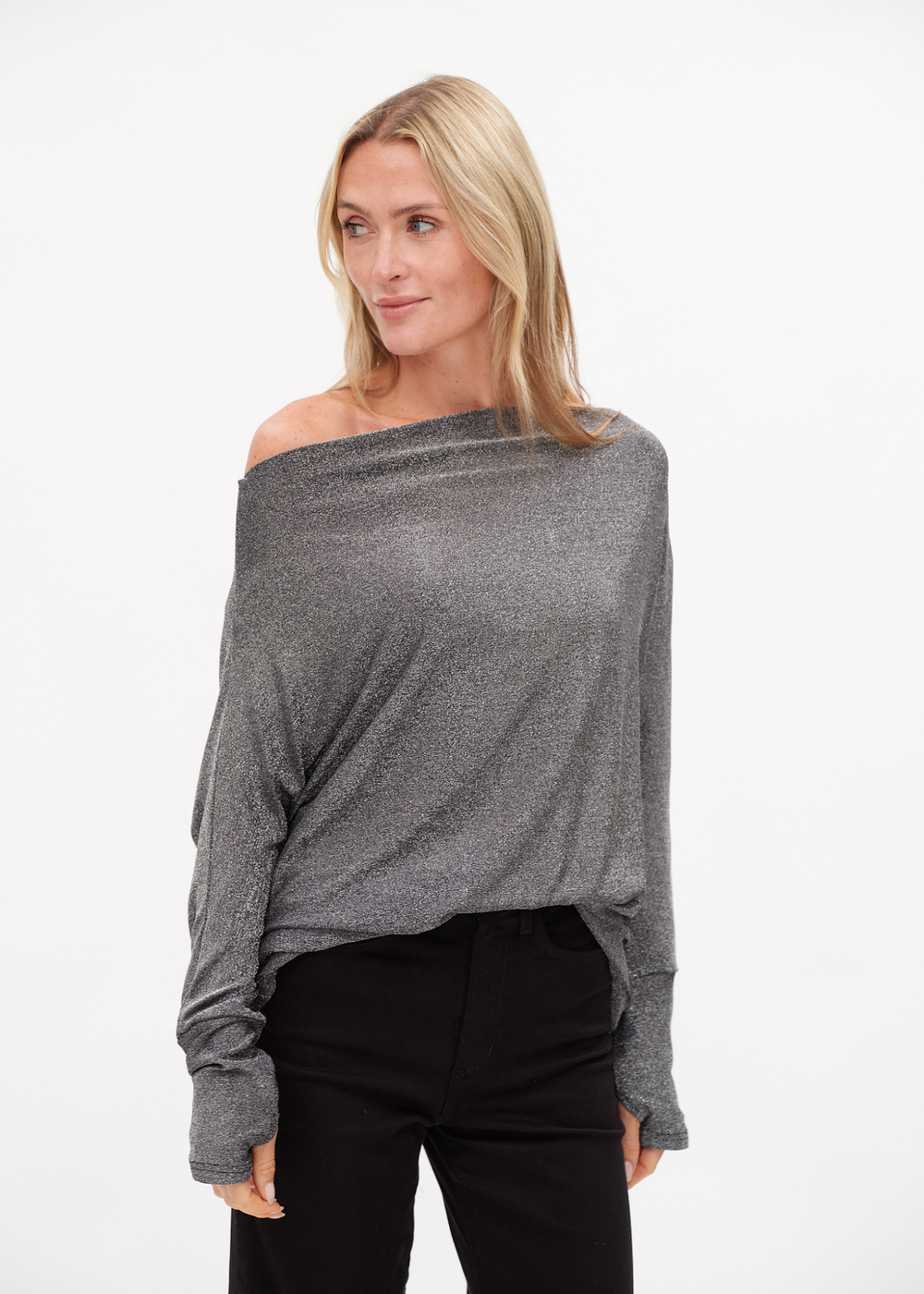 Woman wearing a silver off the shoulder top with black jeans against a white background