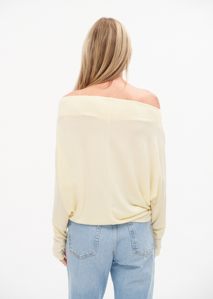 Woman turned around wearing an off the shoulder yellow top with jeans