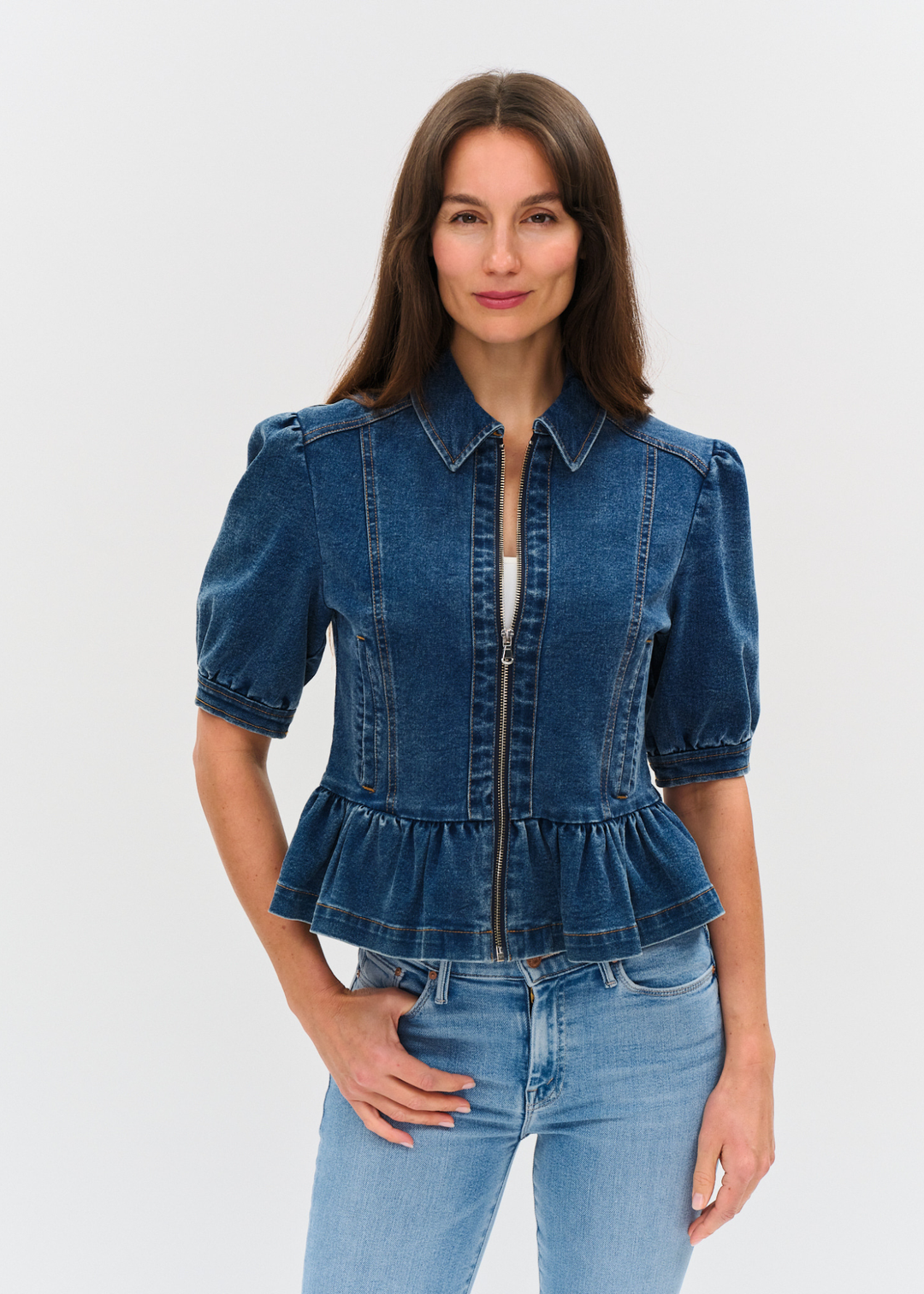 Woman wearing a dark denim jacket with puff sleeves and a peplum design over a white shirt and light wash jeans