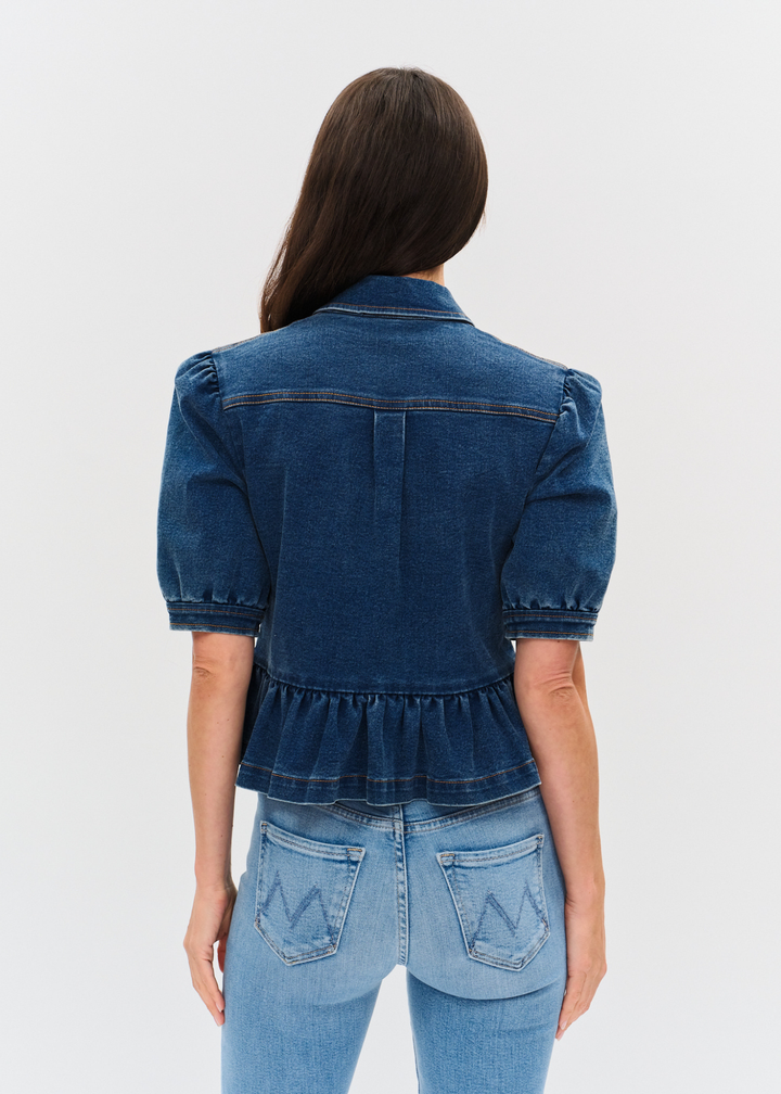 Woman turned around wearing a dark denim jacket with puff sleeves and a peplum design over a white shirt and light wash jeans
