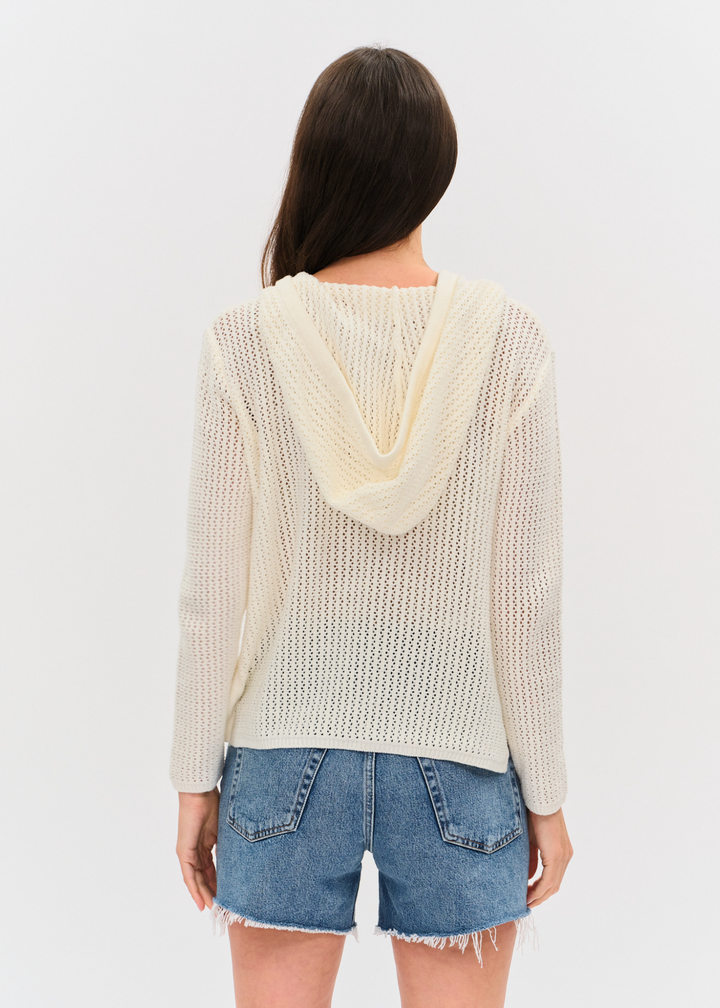 Woman turned around wearing an ivory crochet hoodie with denim shorts