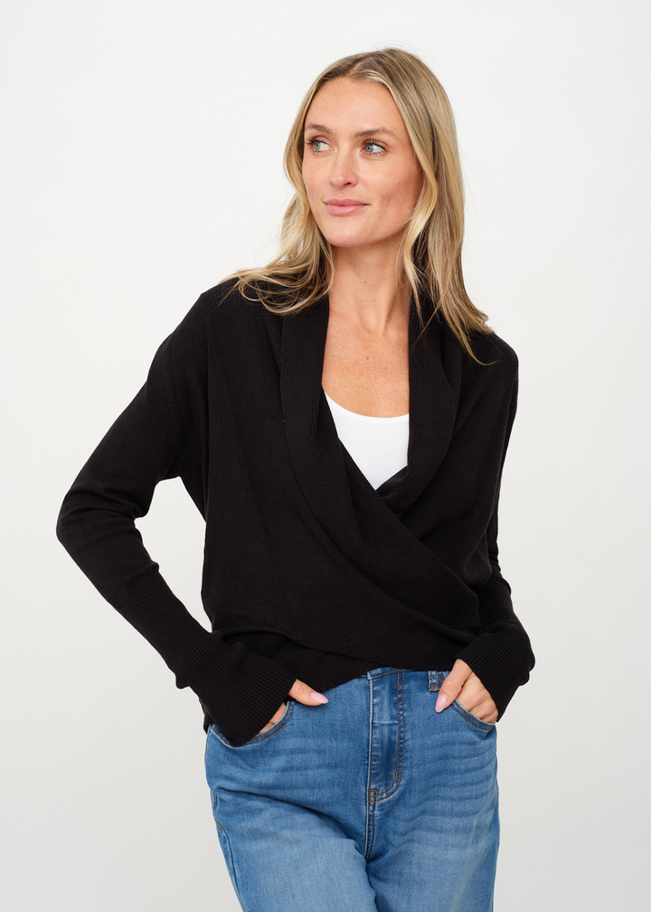 Woman wearing a black cardigan that crosses in the front with jeans in front of a white background