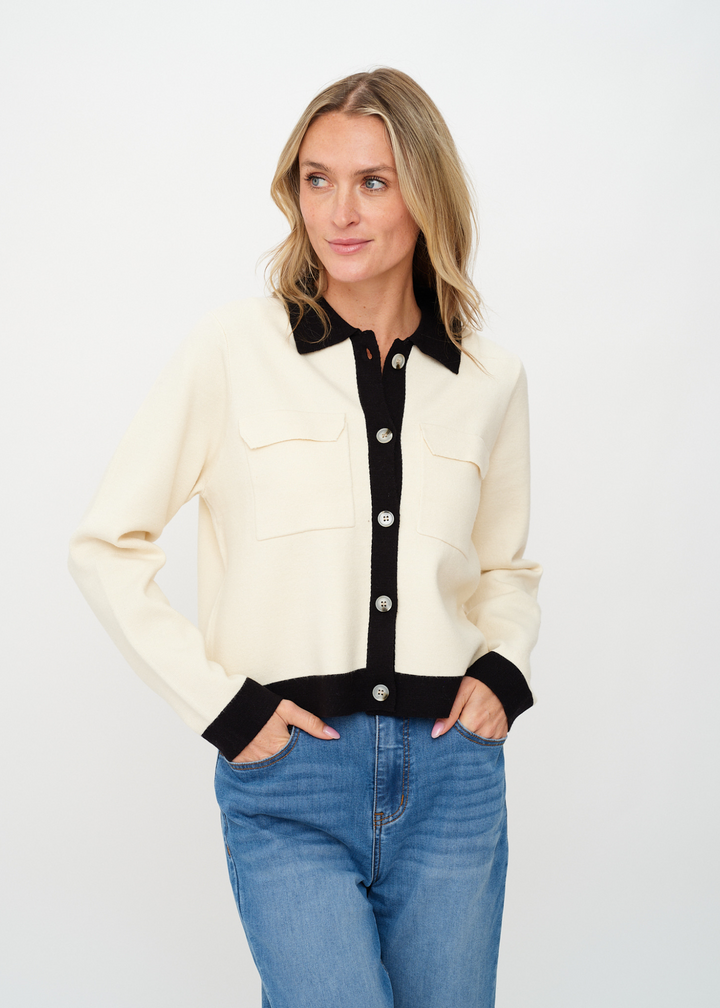 Woman wearing an ivory button up cardigan with a black underlayer and collared neckline in front of a white background