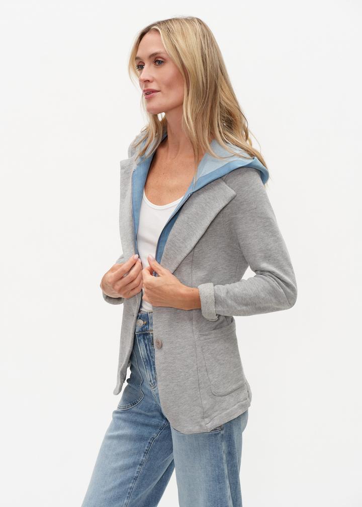 Woman turned to the side wearing a denim and grey knit hooded blazer with jeans