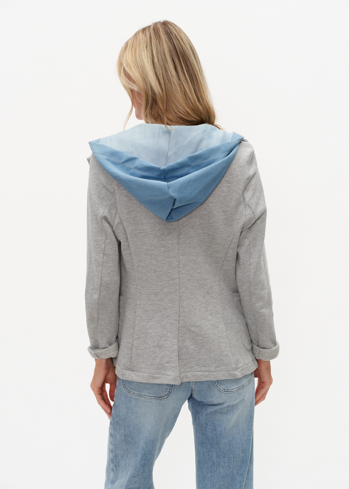 Woman turned around wearing a denim and grey knit hooded blazer with jeans