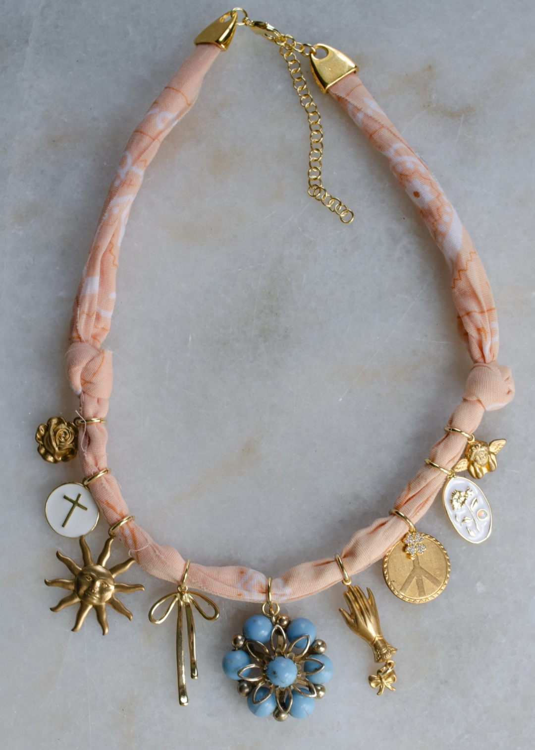 Light pink bandana with gold and multicolor charms against a grey background
