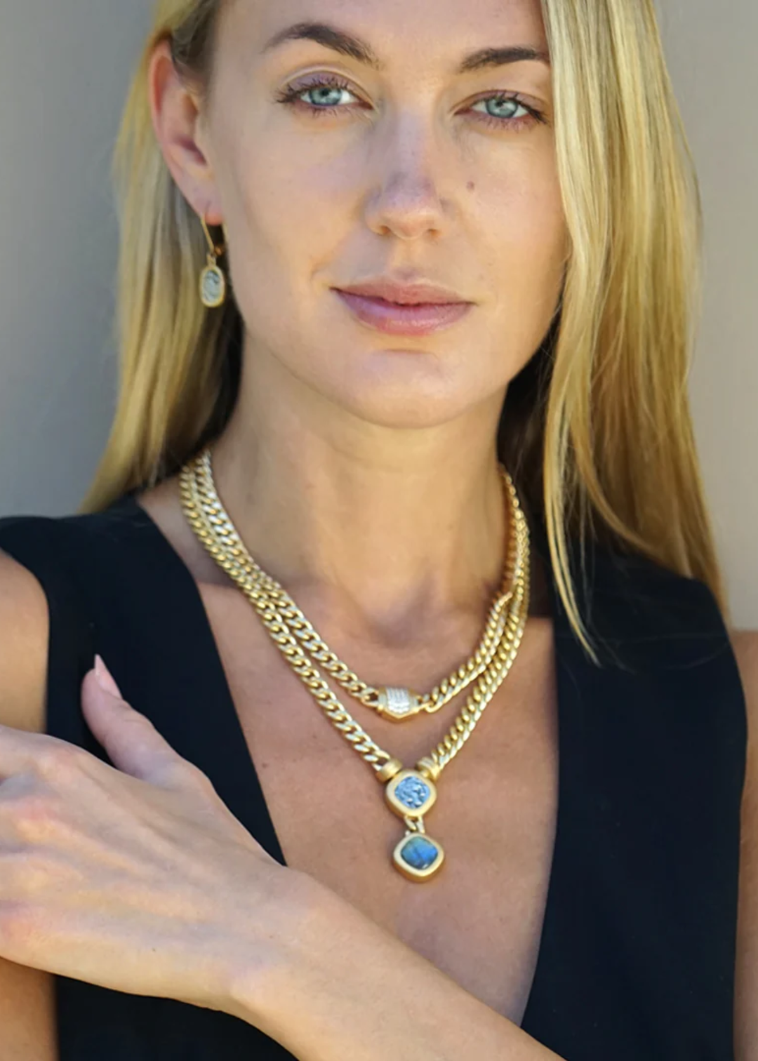 Woman wearing a gold chain necklace with a coin and loabradorite pendant and other jewelry