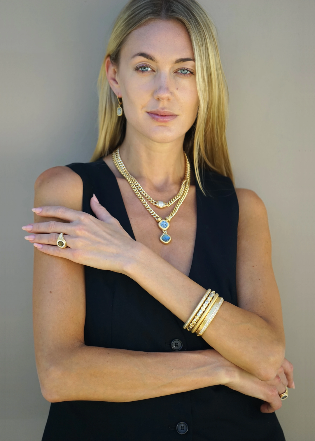 Woman wearing a gold chain necklace with a coin and labradorite pendant and other jewelry