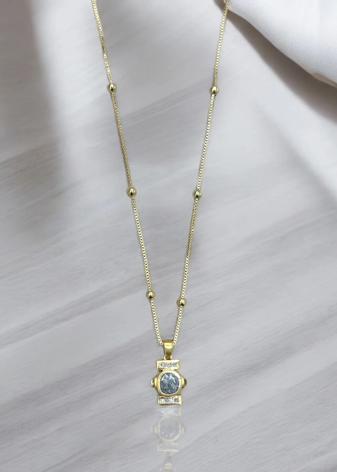 Gold chain necklace with a silver coin pendant surrounded by a gold frame with CZ details on a white background