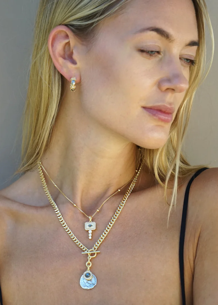 Woman wearing multiple necklaces including a gold pendant necklace with CZ details on a white background