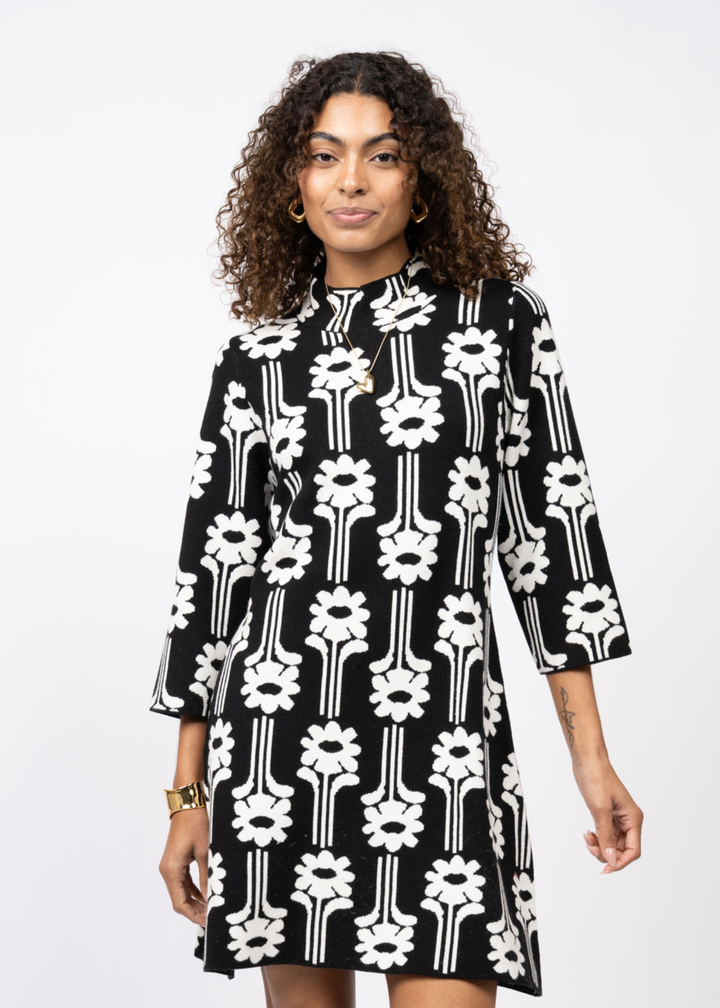 Woman wearing a black dress with a white pattern and 3/4 length sleeves in front of a white background
