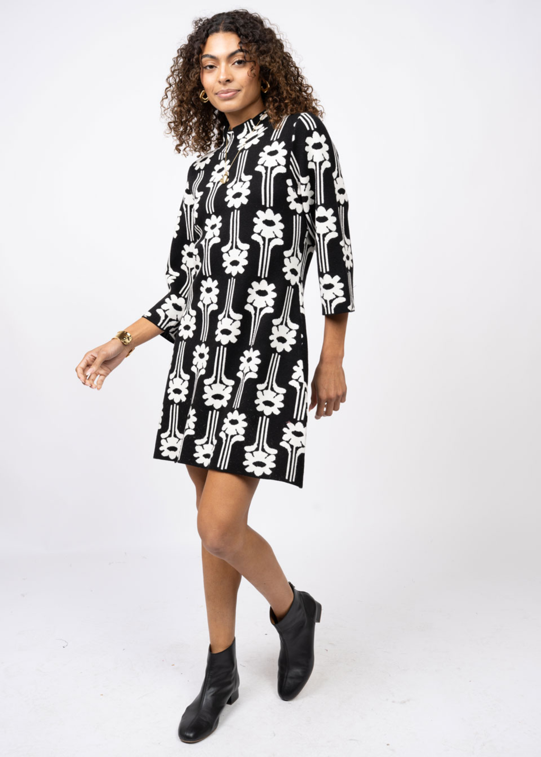 Woman turned to the side wearing a black dress with a white pattern and 3/4 length sleeves in front of a white background