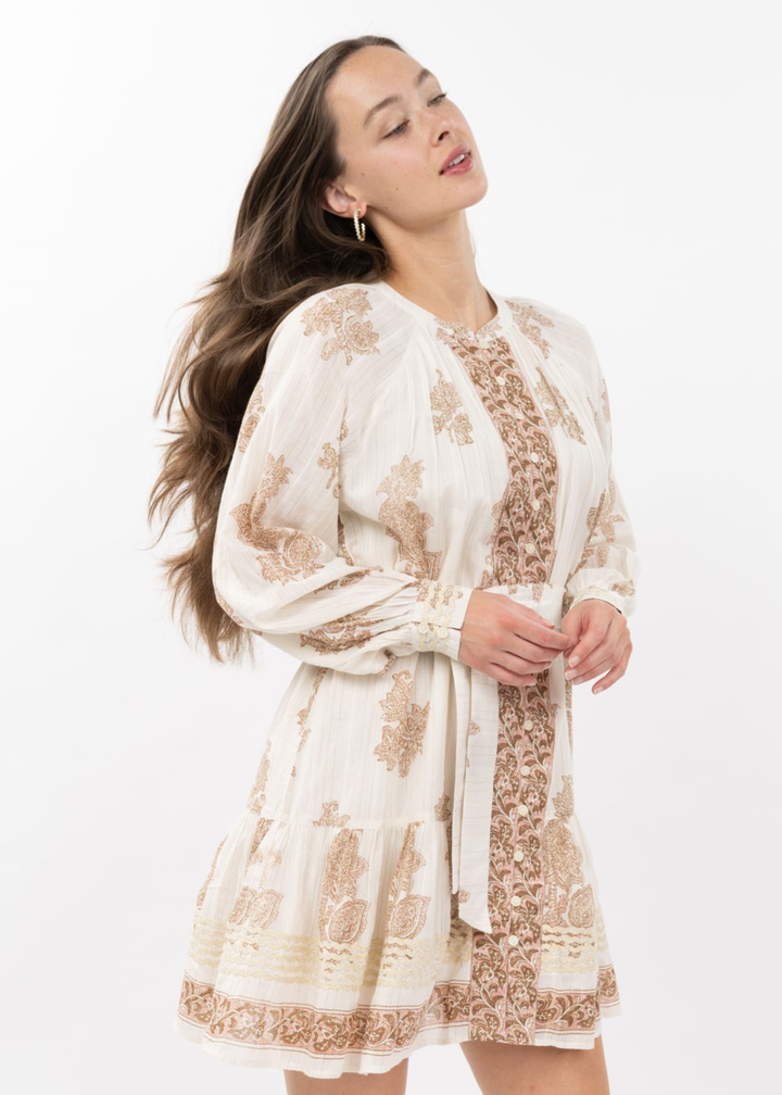 Woman wearing an ivory long sleeve mini dress with a brown floral pattern and a belt